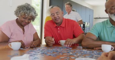Happy senior diverse people playing puzzle at table at retirement home. healthy, active retirement and body inclusivity.