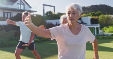 Senior diverse people exercising in garden on sunny day at retirement home. healthy, active retirement and body inclusivity.