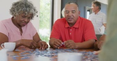 Happy senior diverse people playing puzzle at table at retirement home. healthy, active retirement and body inclusivity.