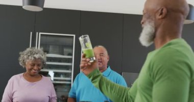 Happy senior diverse people drinking healthy drink in kitchen at retirement home. healthy, active retirement and body inclusivity.