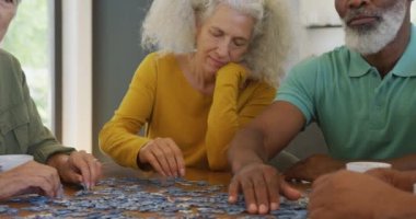 Happy senior diverse people playing puzzle at table at retirement home. healthy, active retirement and body inclusivity.