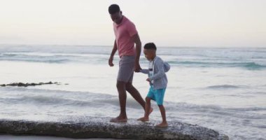 Afrika kökenli Amerikalı baba oğluyla güneşli sahilde yürüyor. sağlıklı ve aktif zaman plaj tatili.