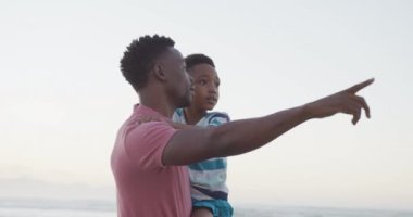 Afrika kökenli Amerikalı baba oğlunu güneşli sahilde taşıyor. sağlıklı ve aktif zaman plaj tatili.