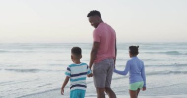 Afrika kökenli Amerikalı baba güneşli sahilde kızlarıyla ve oğluyla yürüyor. sağlıklı ve aktif zaman plaj tatili.