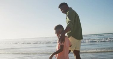 Mutlu Afro-Amerikan babası güneşli sahilde oğluyla yürüyor. sağlıklı ve aktif zaman plaj tatili.