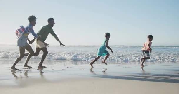 快乐的非洲裔美国夫妇与女儿和儿子在阳光灿烂的海滩上奔跑 健康而活跃的海滨假期 — 图库视频影像