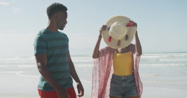 幸せなアフリカ系アメリカ人のカップルが日当たりの良いビーチで帽子を歩く 健康的で活発な時間のビーチホリデー — ストック動画