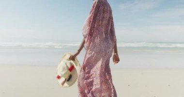 Mutlu Afro-Amerikalı kadın güneşli sahilde şapkasıyla yürüyor. sağlıklı ve aktif zaman plaj tatili.