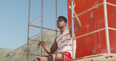 Afrika kökenli Amerikalı erkek cankurtaran güneşli sahildeki kuleyi teftiş ediyor. sağlıklı ve aktif zaman plaj tatili.