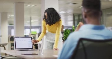 Çift ırklı mutlu iş kadınının dizüstü bilgisayarı kullanırken ve erkek arkadaşla konuşurken videosu. İş adamları ve ofis kavramında çalışmak.