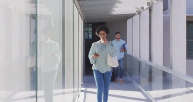 Afro-Amerikan iş kadınının ofisinde akıllı telefon ve kahveyle yürüdüğü bir video. İş adamları ve ofis kavramında çalışmak.