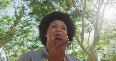 Parkta akıllı telefondan konuşan mutlu ve melez bir kadın. dijital göçebe hareket halinde, beden içeriği.