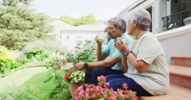 Bahçede kahve içen rahat, çift ırklı yaşlı çiftin videosu. aktif emeklilik yaşam tarzı, kıdemli ilişki ve teknoloji konseptiyle zaman geçirme.