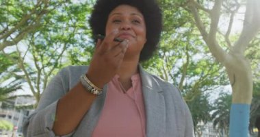 Parkta akıllı telefondan konuşan mutlu ve melez bir kadın. dijital göçebe hareket halinde, beden içeriği.