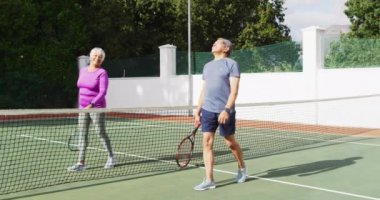 Tenis kortunda raketle yürüyen mutlu son sınıf çifti videosu. aktif emeklilik yaşam tarzı, kıdemli ilişki ve tenis eğitim konsepti.