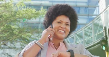 Mutlu ve çift ırklı bir kadın. Akıllı olanı kontrol ediyor ve şehirde yürüyor. dijital göçebe hareket halinde, beden içeriği.