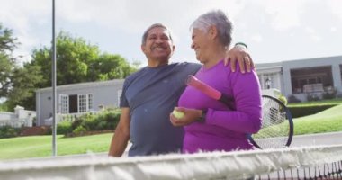 Çift ırklı mutlu çiftin tenis kortunda raketlerle sarılıp yürüdüğü bir video. aktif emeklilik yaşam tarzı, kıdemli ilişki ve tenis eğitim konsepti.