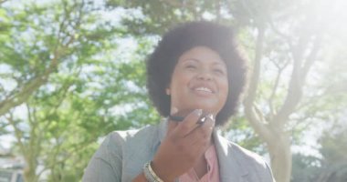 Parkta akıllı telefondan konuşan mutlu ve melez bir kadın. dijital göçebe hareket halinde, beden içeriği.