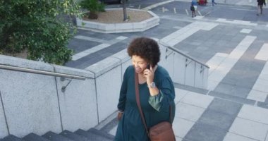 Mutlu ve çift ırklı bir kadın merdivenlerde yürüyor ve akıllı telefondan konuşuyor. dijital göçebe hareket halinde, beden içeriği.