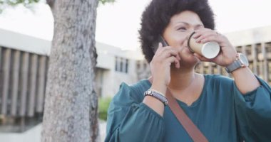 Mutlu ve melez bir kadın akıllı telefonla konuşuyor ve kahve içiyor. dijital göçebe hareket halinde, beden içeriği.