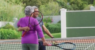 Çift ırklı mutlu çiftin raket tutarken ve tenis kortunu kucaklarken videosu. aktif emeklilik yaşam tarzı, kıdemli ilişki ve tenis eğitim konsepti.