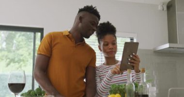 Afro-Amerikalı mutlu çiftin mutfakta tablet kullanarak yemek pişirdiği bir video. Aşk, ilişki, birliktelik ve evde kaliteli zaman geçirme.