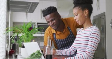 Afro-Amerikalı mutlu çiftin tabletle mutfakta yemek pişirdiği bir video. Aşk, ilişki, birliktelik ve evde kaliteli zaman geçirme.