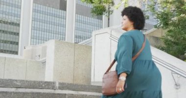 Mutlu ve çift ırklı bir kadın şehirde akıllı telefonuyla merdivenlerde yürüyor. dijital göçebe hareket halinde, beden içeriği.