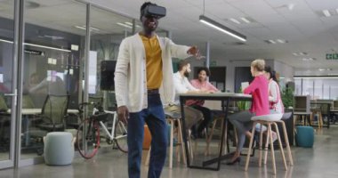 Mutlu Afro-Amerikan iş adamı ofisteki meslektaşlarına karşı kulaklık kullanıyor. Modern bir ofiste çalışmak..