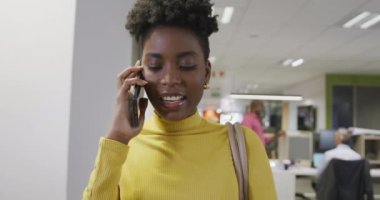 Afro-Amerikan iş kadını akıllı telefondan konuşuyor ve ofiste yürüyor. Modern bir ofiste çalışmak..