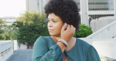 Mutlu ve çift ırklı kadın akıllı telefon kullanıyor ve şehirde kulaklık takıyor. dijital göçebe hareket halinde, beden içeriği.