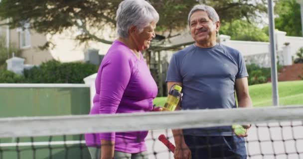 Video Feliz Pareja Ancianos Birraciales Sosteniendo Agua Pelotas Tenis Cancha — Vídeos de Stock