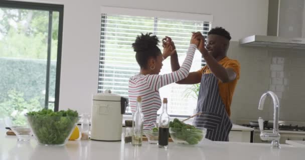 キッチンで一緒に料理をしながら踊る幸せなアフリカ系アメリカ人のカップルのビデオ 家庭で質の高い時間を過ごすことです — ストック動画