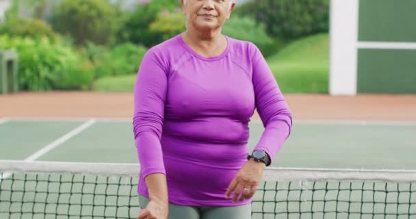 Video Feliz Mujer Mayor Birracial Sosteniendo Raqueta Cancha Tenis Estilo — Vídeo de stock