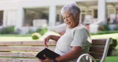 Bahçedeki bankta oturan rahat, melez, son sınıf öğrencisi bir kadının videosu. aktif emeklilik yaşam tarzı, hobi ve dışarıda zaman geçirme.