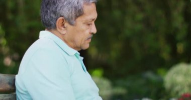 Melez bir adamın kitap okuyup bahçede bankta oturduğu rahat bir video. aktif emeklilik yaşam tarzı, hobi ve dışarıda zaman geçirme.