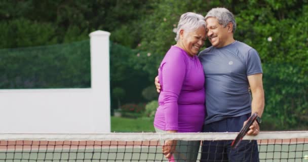 テニスコートでのトレーニング中に抱擁幸せな出産のシニアカップルのビデオ 現役引退生活 シニアリレーションシップ テニストレーニングのコンセプト — ストック動画