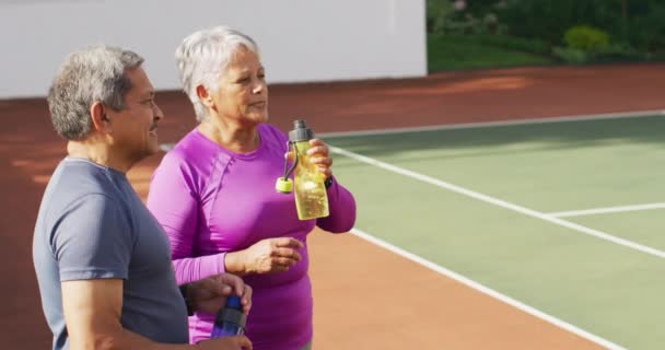 Video Van Gelukkig Biracial Senior Koppel Drinkwater Praten Training Tennisbaan — Stockvideo