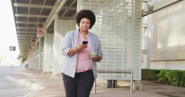 Ditambah Ukuran Birasial Wanita Berjalan Dengan Smartphone Dan Salad Kota — Stok Video