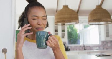 Afro-Amerikalı kadın elinde kahve fincanı tutarak evde akıllı telefondan konuşuyor. Yaşam tarzı ve teknoloji kavramı 