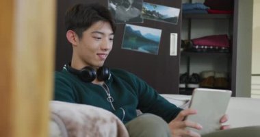 Asyalı çocuk evdeki kanepede dijital tablet kullanıyor. Genç yaşam tarzı ve yaşam konsepti