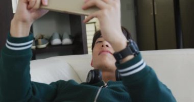 Asyalı çocuk evdeki kanepede uzanmış dijital tablette oyun oynuyor. Genç yaşam tarzı ve yaşam konsepti