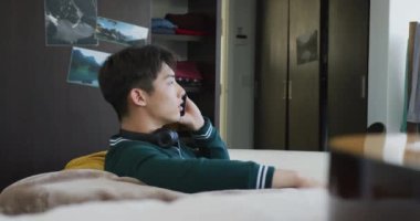 Asyalı çocuk akıllı telefondan konuşuyor. Evdeki kanepede oturuyor. Genç yaşam tarzı ve yaşam konsepti