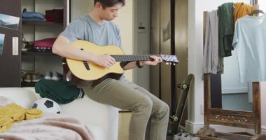 Asyalı çocuk evdeki kanepede gitar çalıyor. Genç yaşam tarzı ve yaşam konsepti