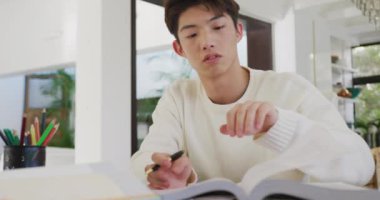 Düşünceli Asyalı genç çocuk evdeki oturma odasında ders çalışıyor. Genç yaşam tarzı ve yaşam konsepti