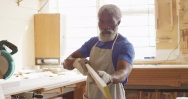 African american male carpenter looking and choosing wooden plank in a carpentry shop. carpentry, craftsmanship and handwork concept