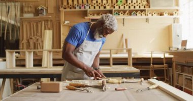 Afro-Amerikan erkek marangoz, marangozhanede keskiyle odun kesen bir önlük takıyor. Marangozluk, işçilik ve el işi konsepti