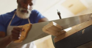 Afrikalı Amerikalı erkek marangoz marangoz bir marangozhanede el testeresi kullanarak tahta kesiyor. Marangozluk, işçilik ve el işi konsepti