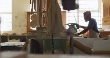 Afrikalı Amerikalı erkek marangoz bir marangozhanede elektrikli testereyle tahta kesiyor. Marangozluk, işçilik ve el işi konsepti