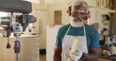 Afrikalı Amerikalı erkek marangoz bir marangozhanede lazer matkapla odun deliyor. Marangozluk, işçilik ve el işi konsepti